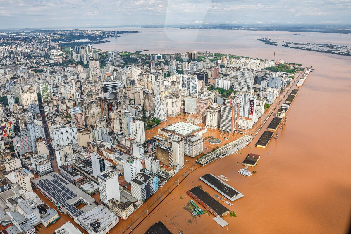 An aerial image of flooding in Canaos, Rio Grande do Sul. Light brown water overflows from a river delta into a city, flooding roads and surrounding buildings.