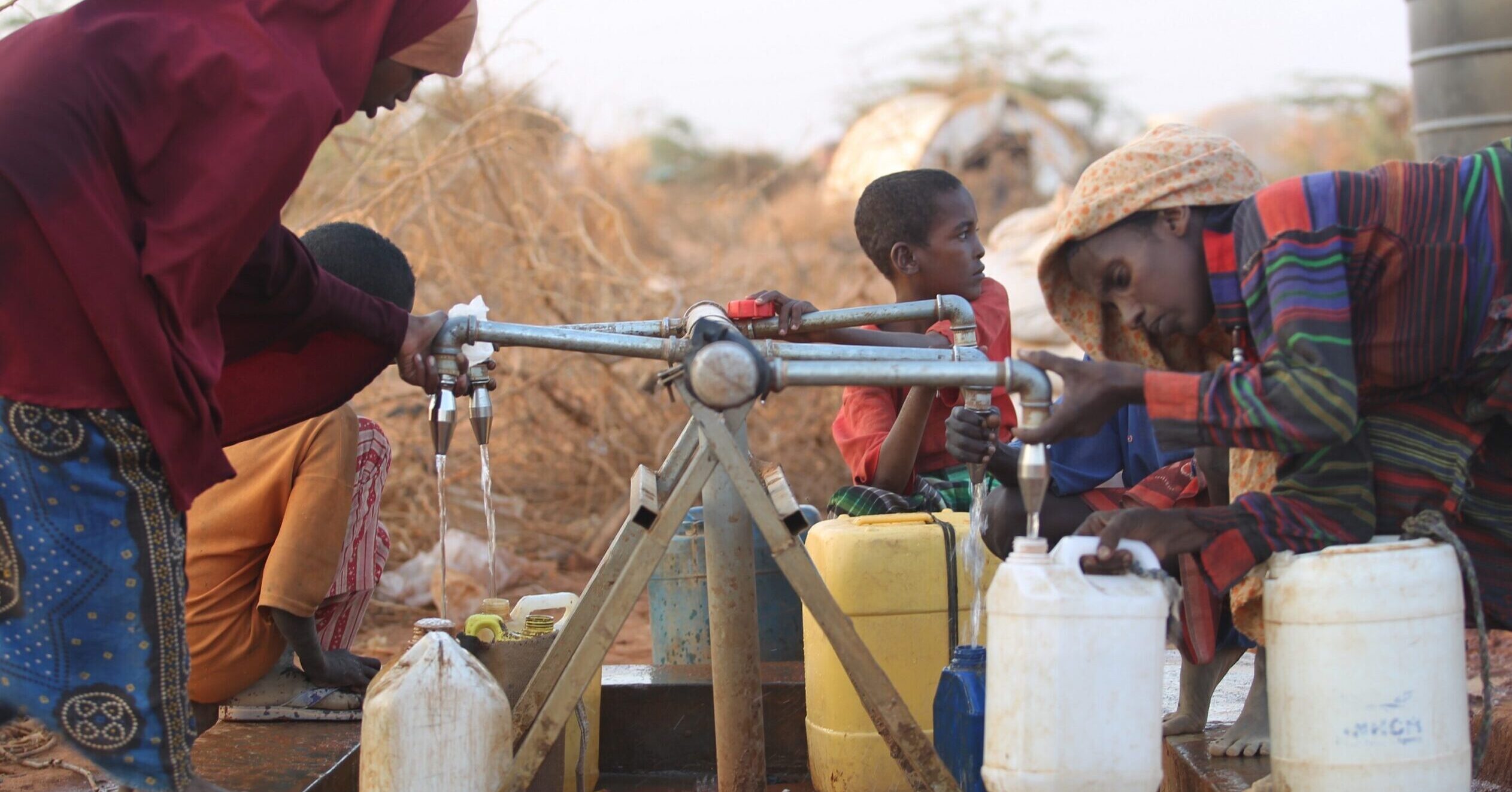 Two women fill up water containers in a refugee camp in Somalia.