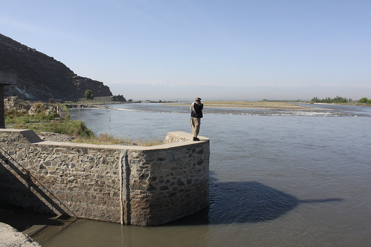 A man stands on top of a concrete flood bank by a river in Afghanistan.
