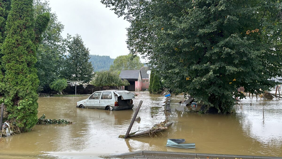 A photo of a flood in the Czech Republic with brown floodwater, a tree and a white car half underwater.